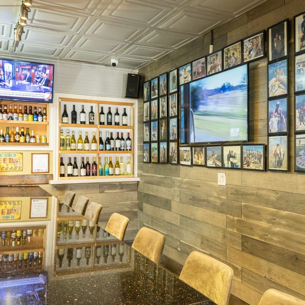 A bar area with a long counter, bar stools, TVs, and shelves of wine and beer.