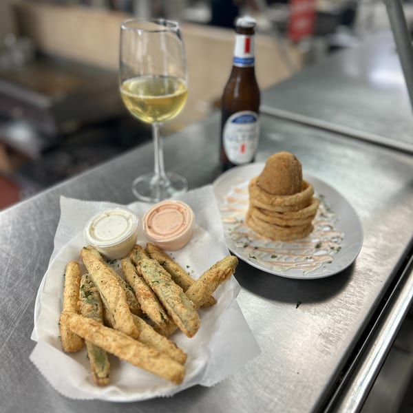 Fried pickles with dipping sauces, onion rings, a glass of white wine, and a beer bottle.