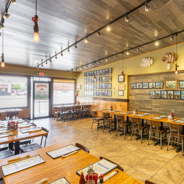 Interior of Cajun Greek restaurant with wooden tables, chairs, and nautical-themed decor on the walls.
