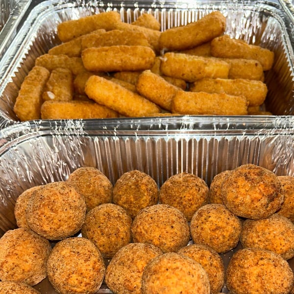 Two foil trays filled with golden-brown fried appetizers: mozzarella sticks and arancini balls.