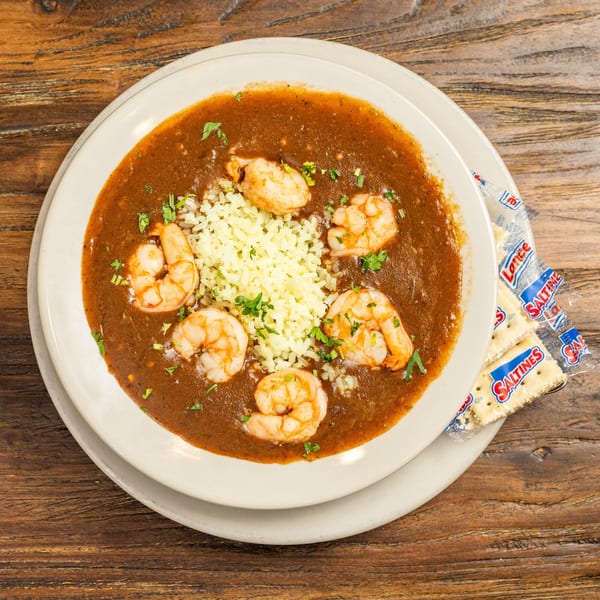 Shrimp gumbo with rice and parsley in a white bowl, with Saltine crackers on a wooden table.