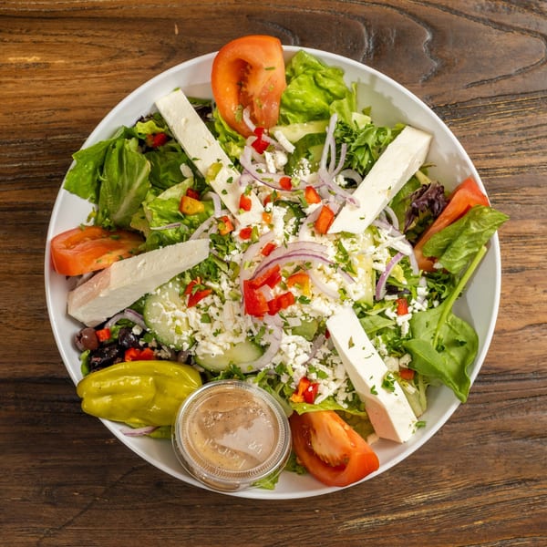 Overhead view of a vibrant Greek salad with feta, tomatoes, olives, and dressing.