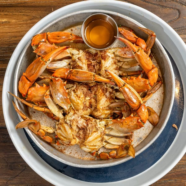 Steamed blue crabs seasoned with spices and served with a side of melted butter in a metal pan.