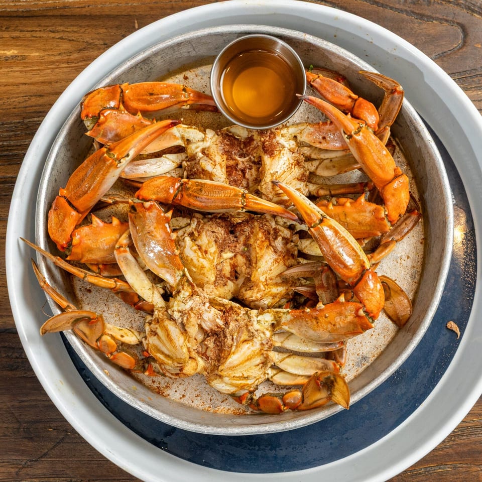 Steamed blue crabs seasoned with spices and served with a side of melted butter in a metal pan.
