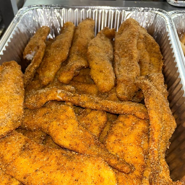 Close-up of golden-brown fried fish fillets, seasoned with spices, in a silver foil pan.