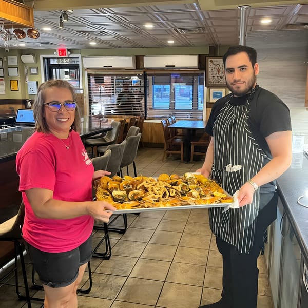 Two restaurant staff members holding a large tray piled high with fried seafood and lemons.