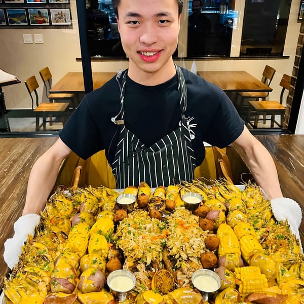 A smiling server presents a large tray of seafood boil with shrimp, corn, potatoes, and crab.
