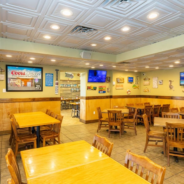 A casual restaurant dining room with wooden tables and chairs, light green walls, and beach-themed decor.