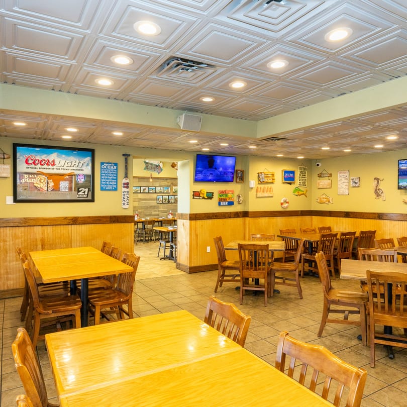 A casual restaurant dining room with wooden tables and chairs, light green walls, and beach-themed decor.