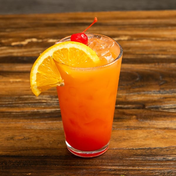 Vibrant orange and red cocktail garnished with an orange slice and a cherry on a wooden table.