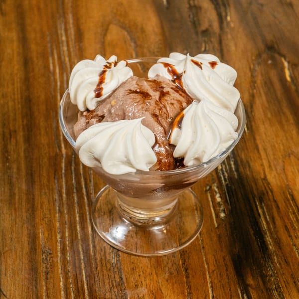 Chocolate ice cream with whipped cream and chocolate syrup in a glass dish on a wooden table.