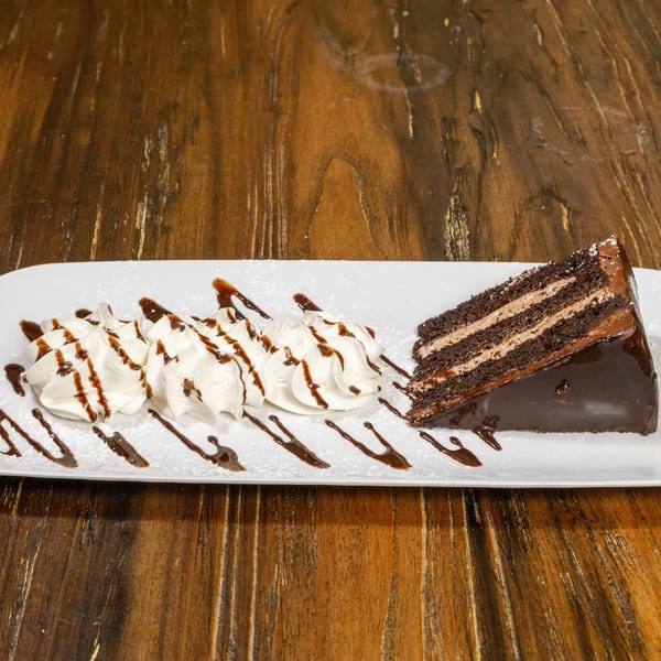 A slice of chocolate cake with whipped cream and chocolate drizzle on a white plate.