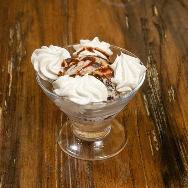 Ice cream sundae with chocolate drizzle and whipped cream in a glass bowl on a wooden table.
