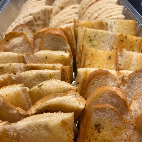 Close-up of golden-brown garlic bread slices arranged in rows within a clear container.