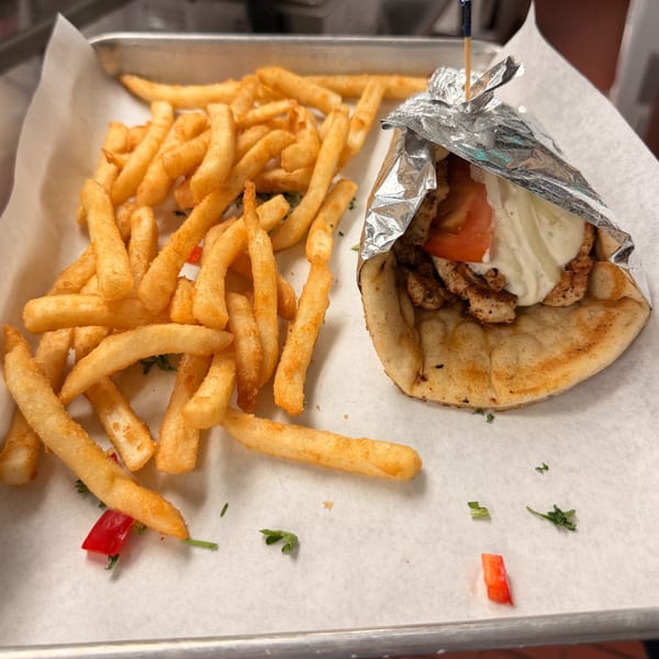 Chicken gyro with tomatoes and white sauce, wrapped in foil, served with golden french fries.