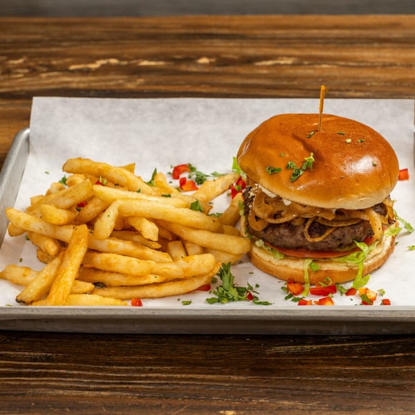 A juicy burger with caramelized onions and a side of golden fries on a metal tray.