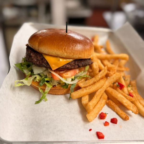 Cheeseburger with lettuce, tomato, onion, and a side of french fries with red pepper flakes.