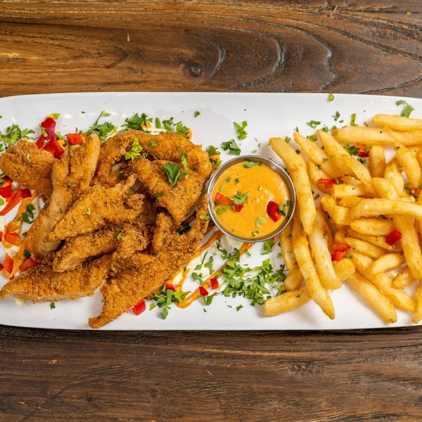 Crispy fried chicken tenders with french fries, a side of dipping sauce, and garnished with parsley and red peppers.