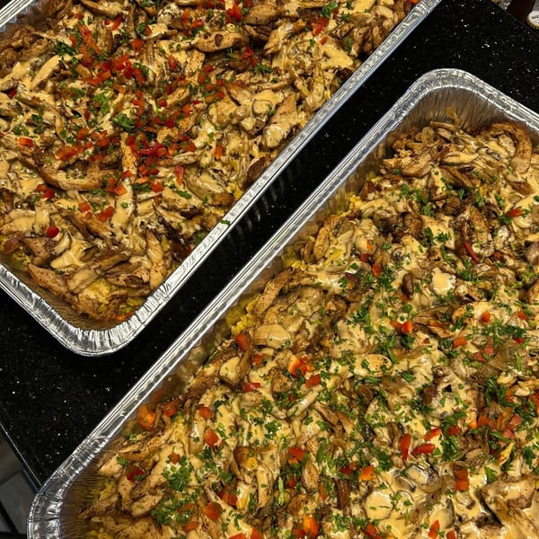 Two foil trays filled with chicken, mushrooms, and rice, topped with sauce, red peppers, and parsley.
