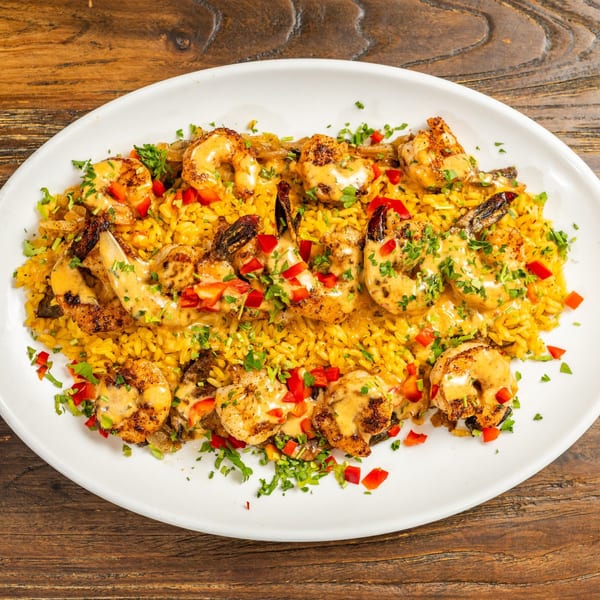 Grilled shrimp and yellow rice with red bell peppers, parsley, and creamy sauce on a white plate.