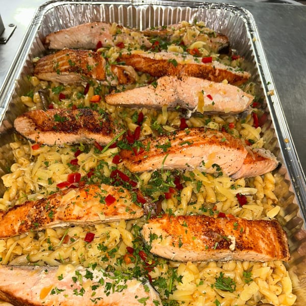 Baked salmon fillets with pasta, red peppers, and parsley in a foil pan.