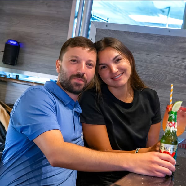 A smiling couple poses for a photo at a restaurant table with drinks.
