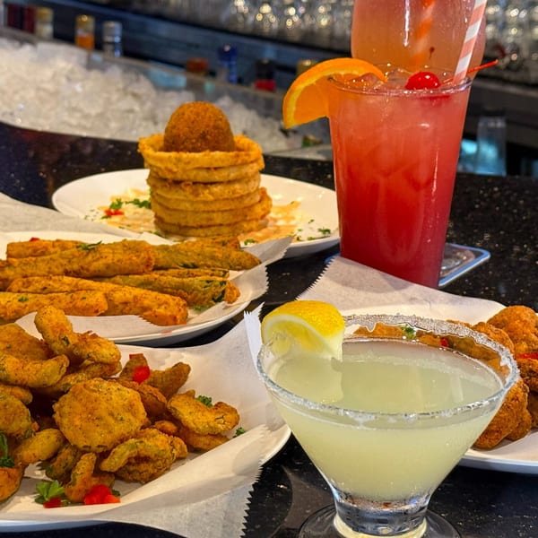Fried pickles, fried okra, onion rings, and two cocktails on a bar counter.