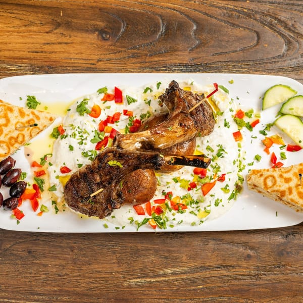Grilled lamb chops with tzatziki, red peppers, parsley, olives, cucumbers, and pita bread.