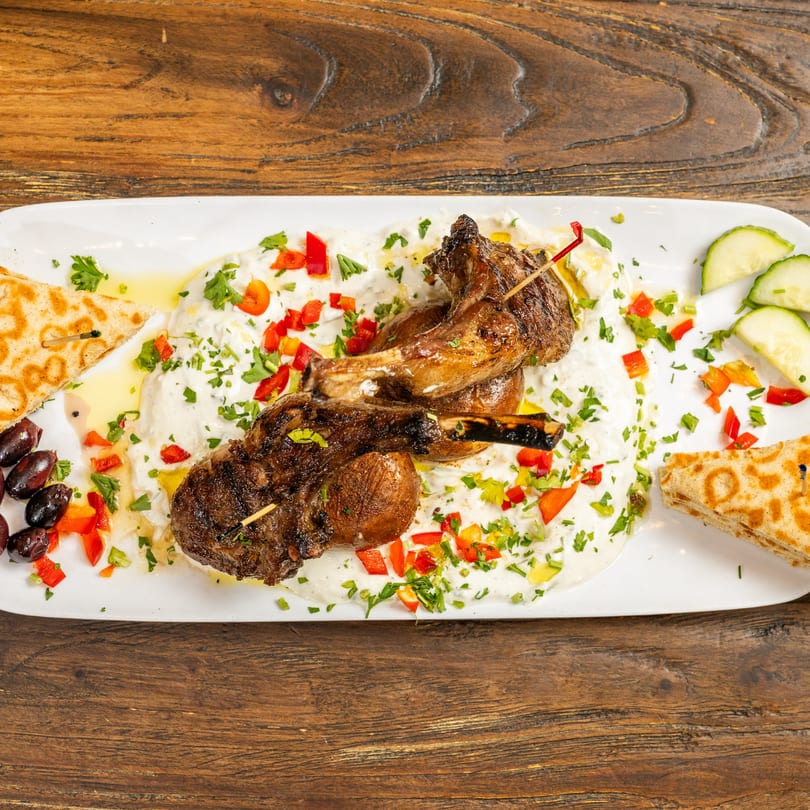 Grilled lamb chops with tzatziki, red peppers, parsley, olives, cucumbers, and pita bread.