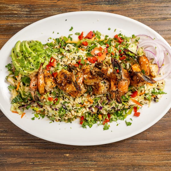 Grilled shrimp skewers on a bed of colorful coleslaw with avocado slices and red onion.