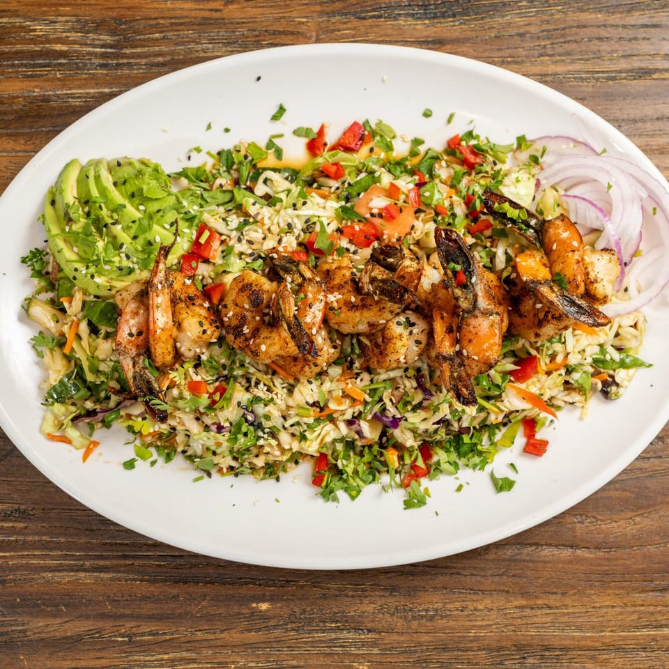 Grilled shrimp skewers on a bed of colorful coleslaw with avocado slices and red onion.
