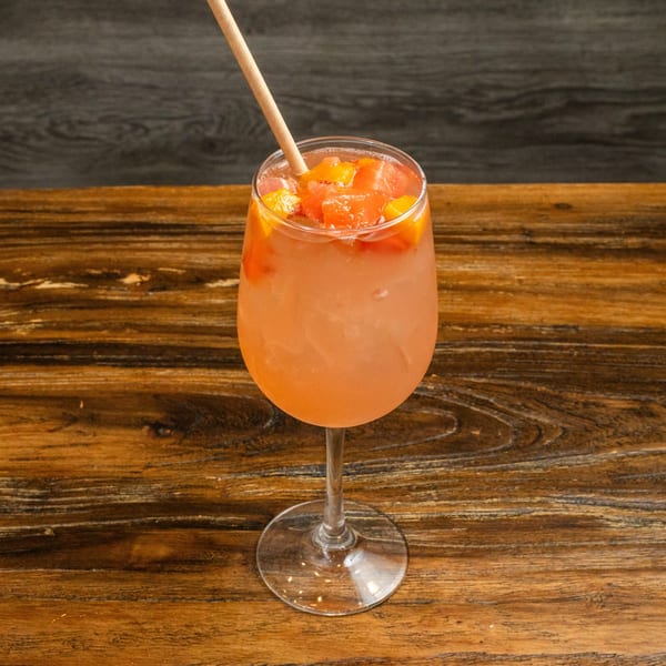 A refreshing pink cocktail with fruit chunks and a straw, on a rustic wooden table.
