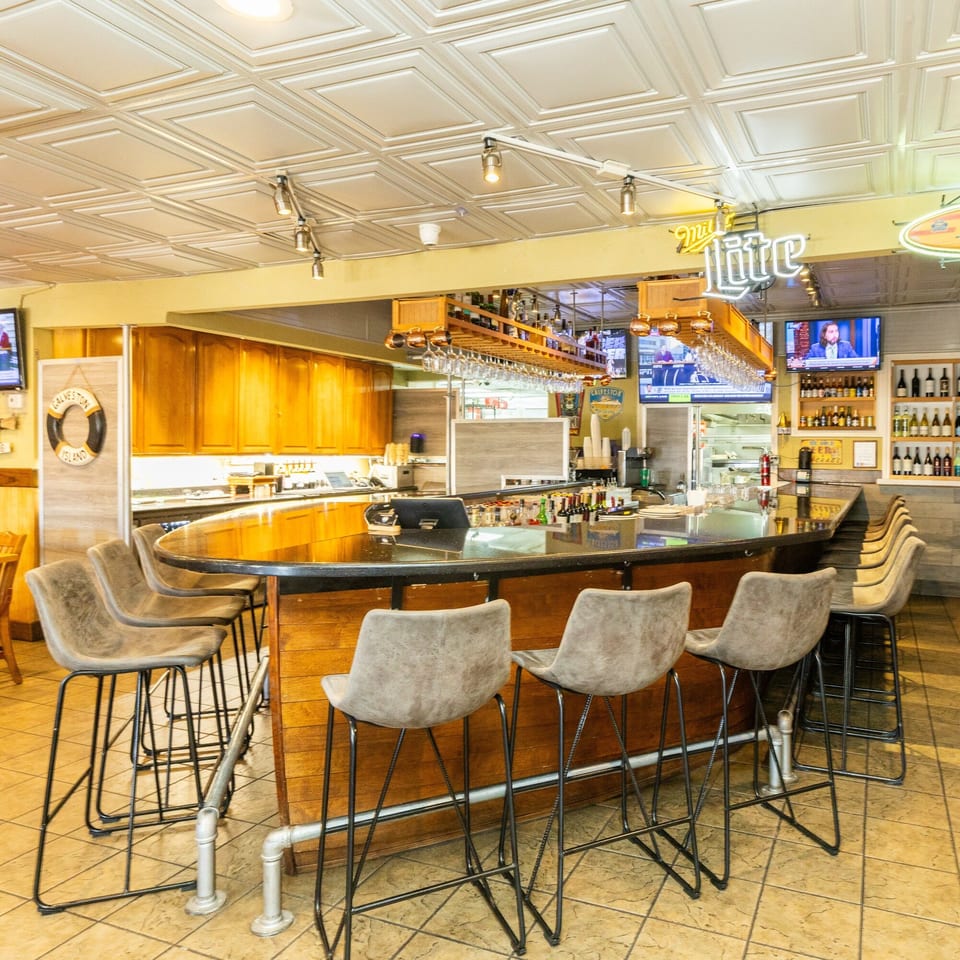 A well-lit, empty restaurant bar with a dark countertop, bar stools, and a Miller Lite neon sign.