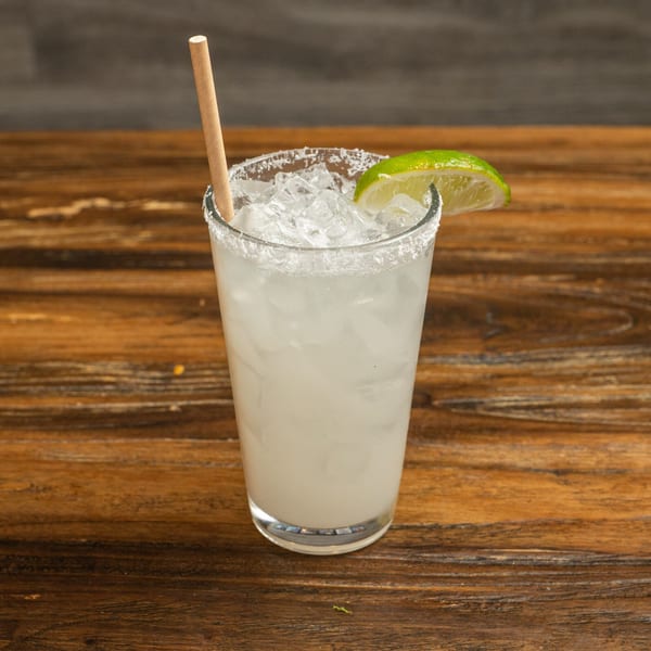 A margarita with a salted rim, lime wedge, and paper straw sits on a wooden table.