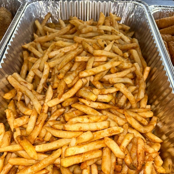 Close-up of a large aluminum tray filled with golden-brown, seasoned french fries.