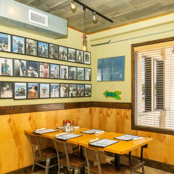 A restaurant dining area with light yellow walls, wood paneling, and framed fishing photos.