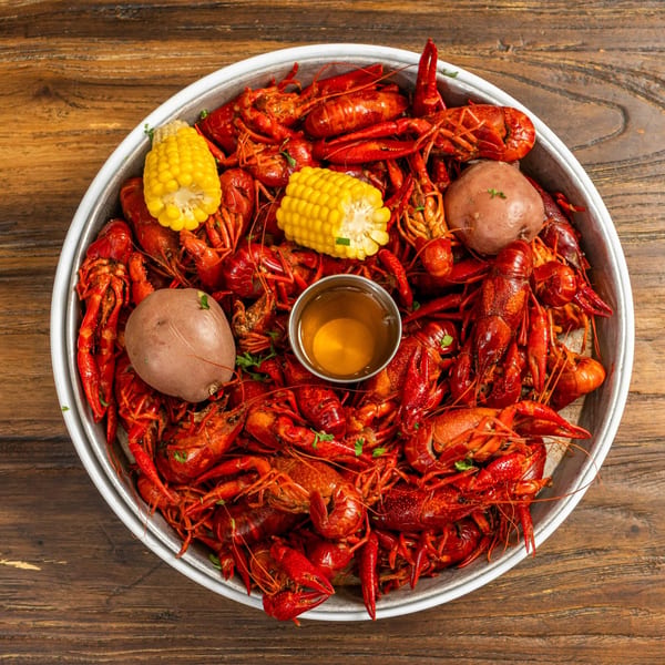 A large metal bowl filled with bright red crawfish, corn on the cob, potatoes, and a dipping sauce.