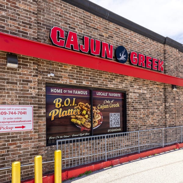 The exterior of Cajun Greek restaurant with a large sign and window advertisements for their B.O.I. Platter.