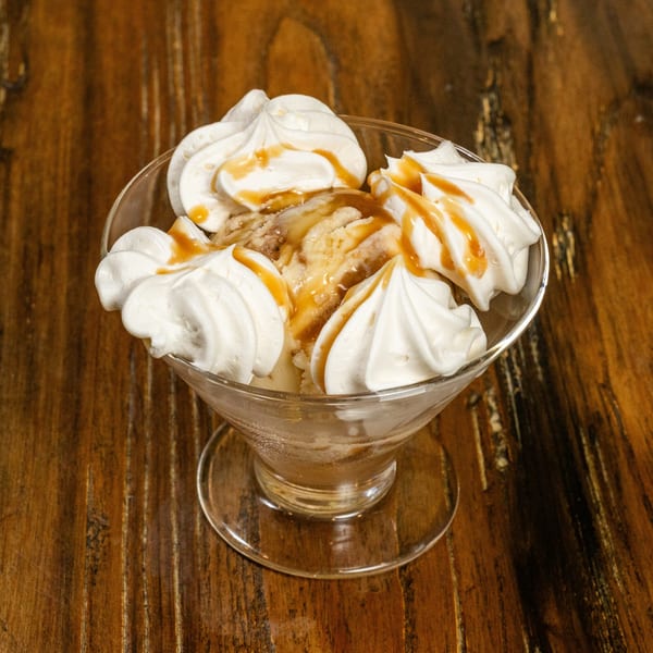 Vanilla ice cream sundae with whipped cream and caramel drizzle in a glass dish on a wooden table.