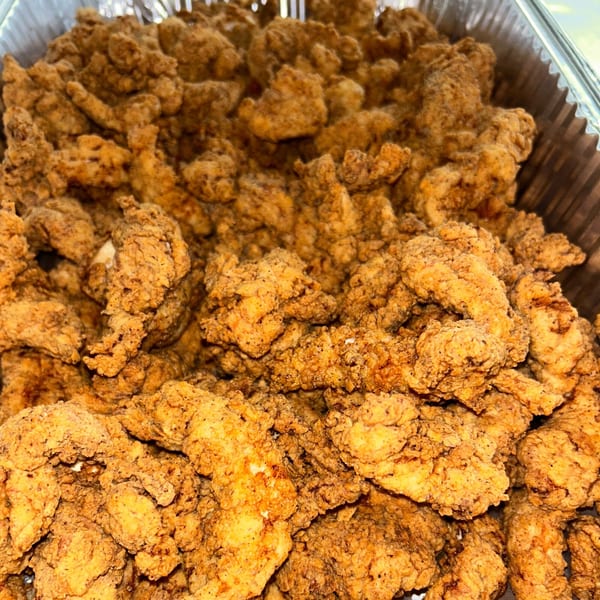 Close-up of a large catering tray filled with golden-brown, crispy fried chicken pieces.