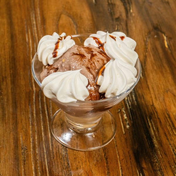 Chocolate ice cream with whipped cream and chocolate syrup in a glass dish on a wooden table.