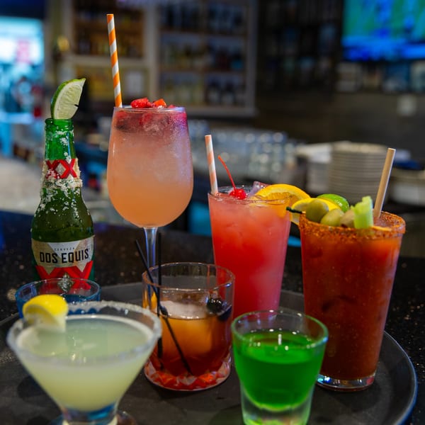 A tray of colorful cocktails, including margaritas, a Michelada, and a Dos Equis beer.