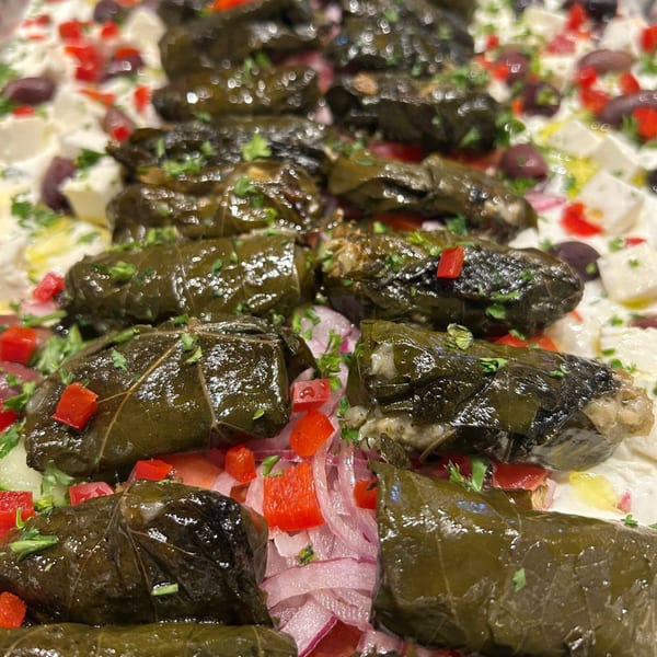Close-up of dolmades (stuffed grape leaves) garnished with red peppers, onions, and parsley.