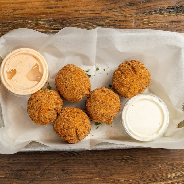 Five breaded, fried balls with two dipping sauces in plastic cups on white paper.
