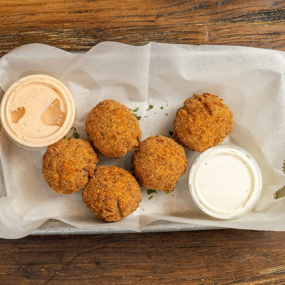 Five breaded, fried balls with two dipping sauces in plastic cups on white paper.
