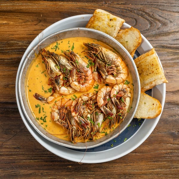 Shrimp in a creamy orange sauce with parsley, served in a metal pan with toasted bread.