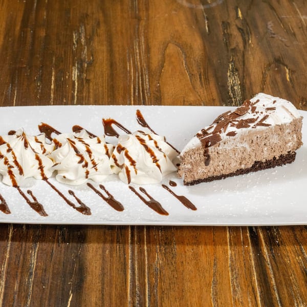 A slice of chocolate mousse pie with whipped cream and chocolate drizzle on a white plate.