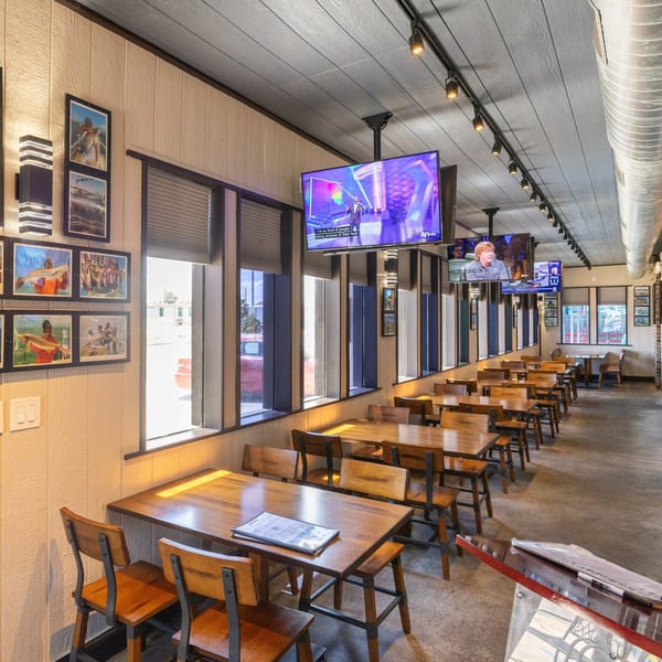 A long, narrow dining room with wooden tables and chairs, TVs, and framed pictures on the walls.