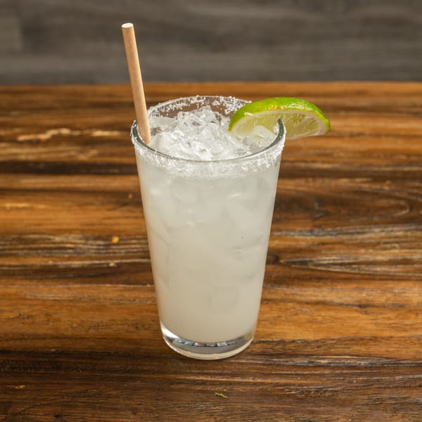 A refreshing margarita with a salted rim, lime wedge, and paper straw on a wooden table.