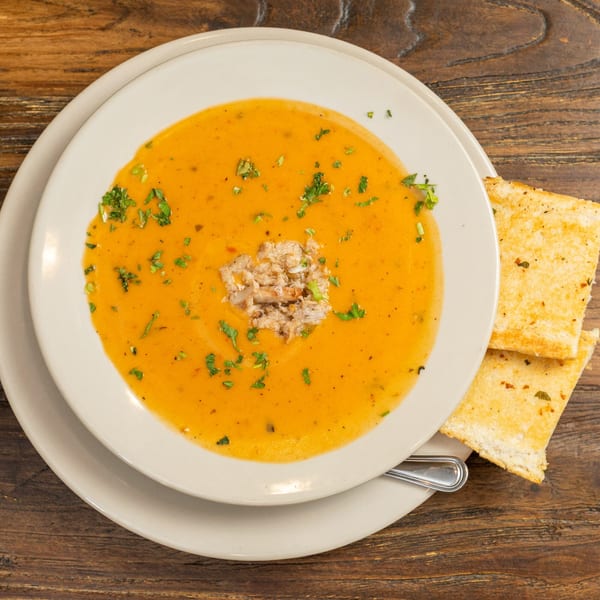 Creamy orange soup with crab meat and parsley, served with toasted bread on a wooden table.